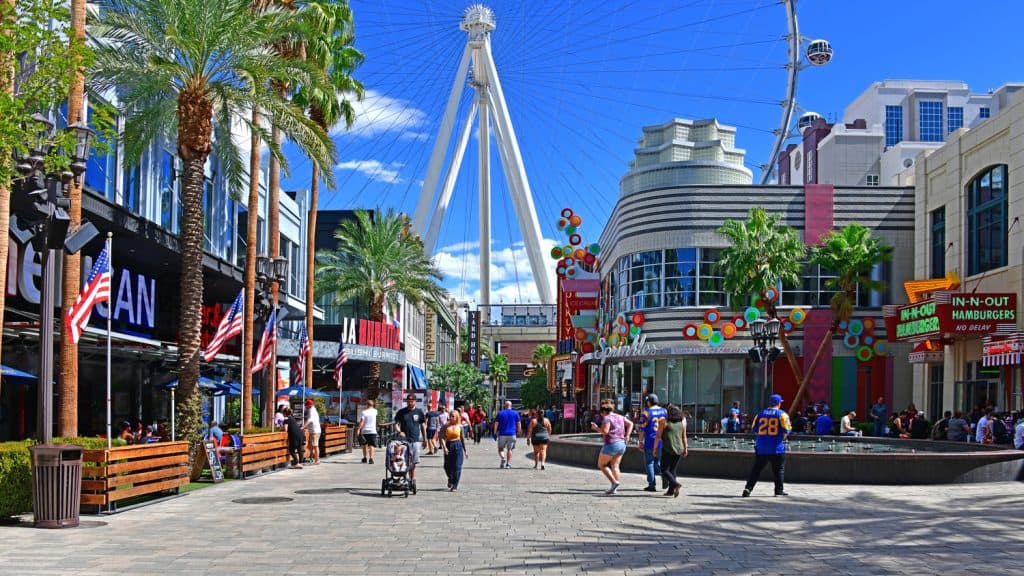 People walking in a large plaza with stores and restaurants in it. 