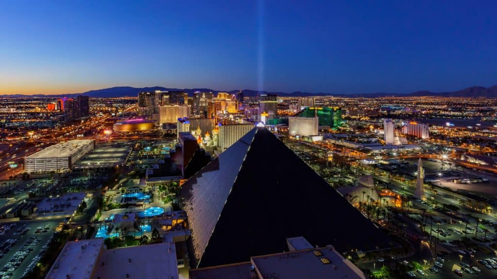 A pyramid shaped hotel with a light beam coming from the top and the Las Vegas strip behind.