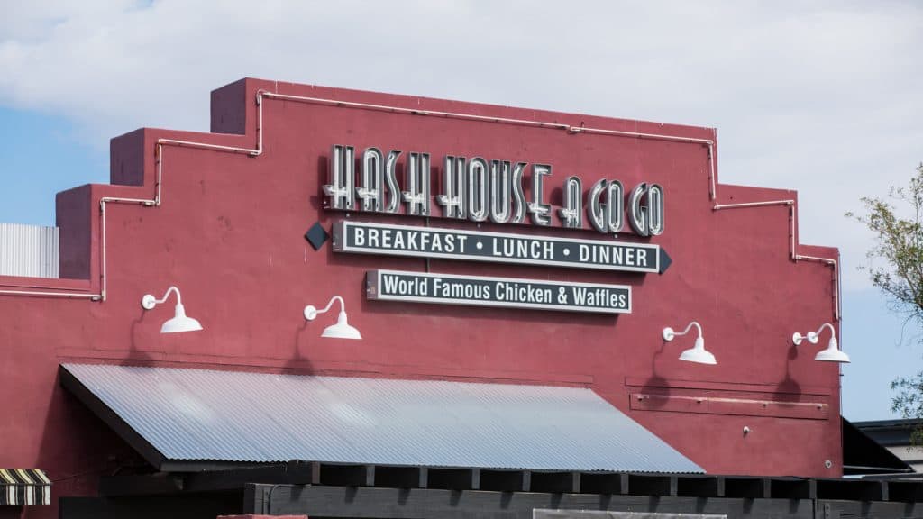 The front of a red building with a sign on top that reads "Hash House A Go Go. Breakfast, Lunch, Dinner. World Famous Chicken & Waffles".