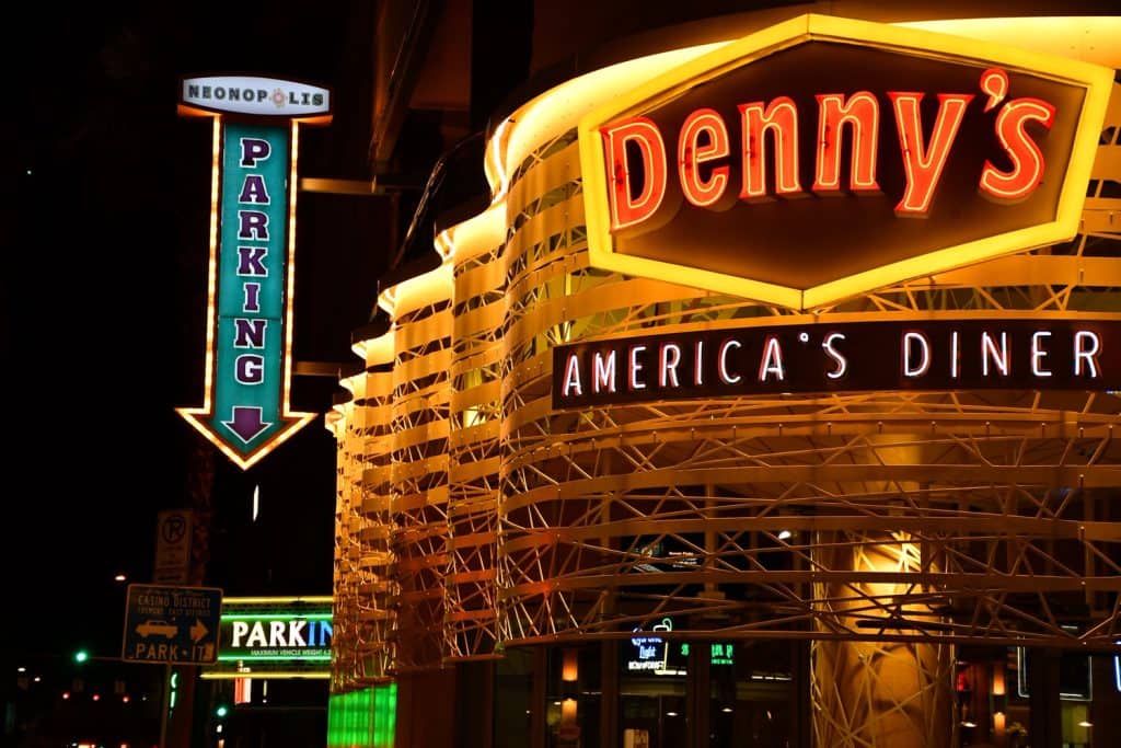 A large light up sign that reads "Denny's. America's Diner" with a sign on the left pointing towards parking.