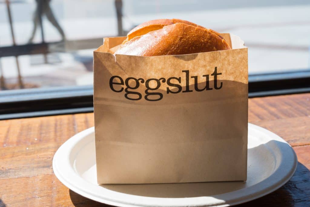 A bagel sticking out of a brown paper bag that says "eggslut" on it.