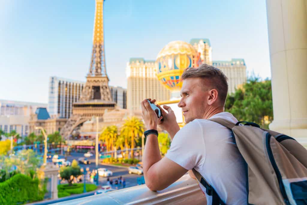 Man smiles while holding his phone next to the Paris hotel in Las Vegas.