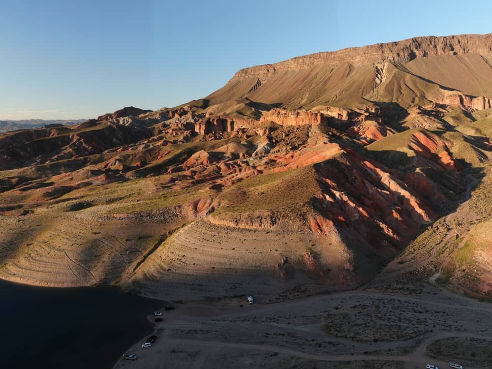 An aerial view of a rocky, desert area with cars parked at the bottom. 